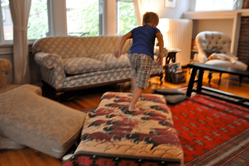 Child with an occupational therapist using pillows and blankets to create an obstacle course at home. 