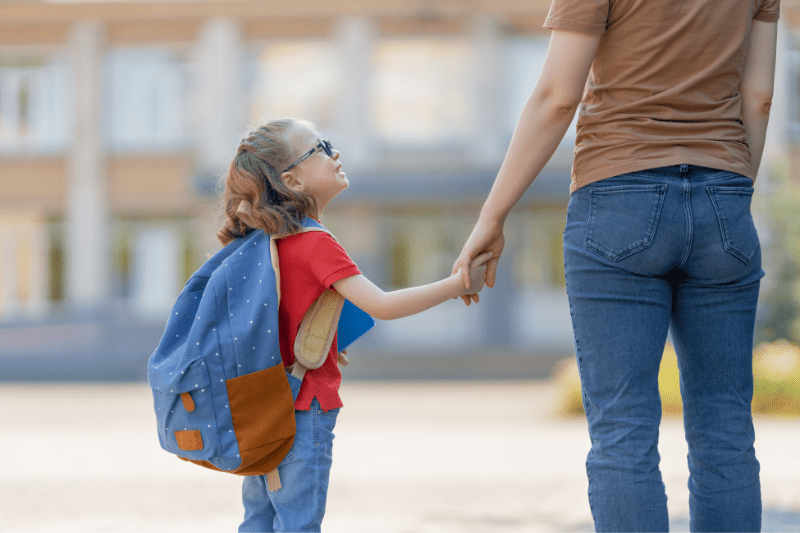 A woman and a young girl clasp hands, symbolizing love and guidance on the kid's first day of school.