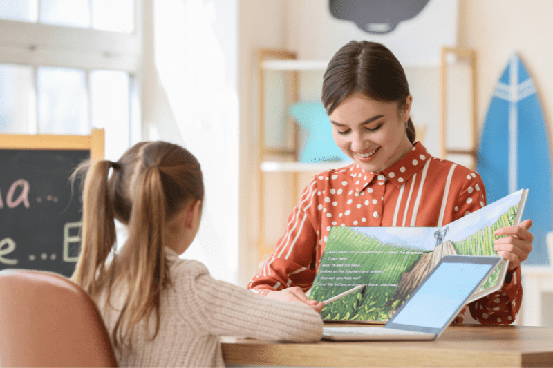 Child and speech therapist reading a book together during a therapy session.