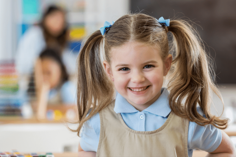 A cheerful girl in a school uniform smiles brightly, celebrating her first day of school in Australia.