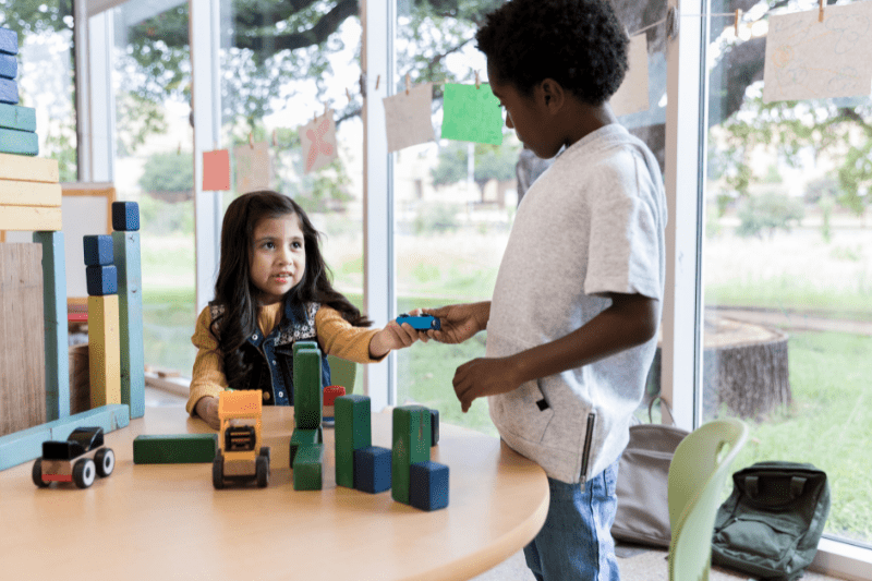 Two children with good play skills sharing toys and smiling.