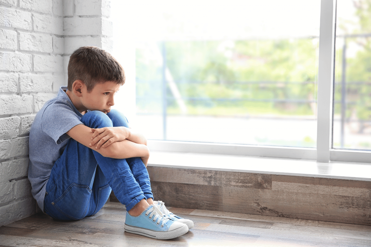 Primary school boy sitting alone by a window looking worried and withdrawn, representing anxiety in children and anxious child behaviour