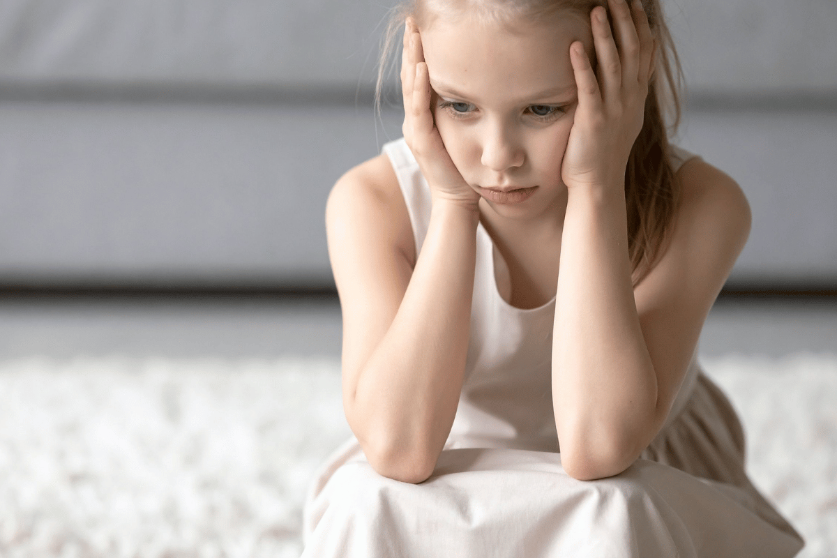 Young girl sitting with her head in her hands looking overwhelmed and worried, representing child anxiety symptoms and emotional distress in children