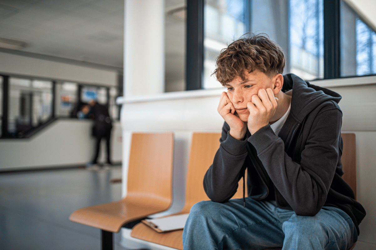 Teen boy sitting with his face in his hands looking flat and overwhelmed, showing how anxiety in older children can look quiet, tired and shut down.